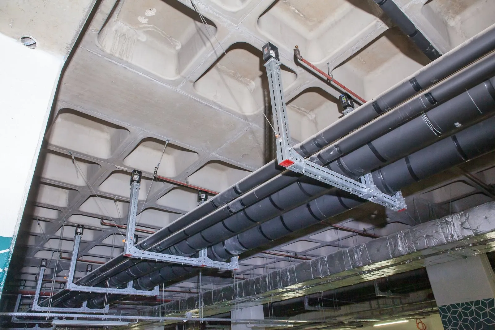 Insulated pipework on spring-isolated trapezes, restrained to a waffle slab with seismic cables