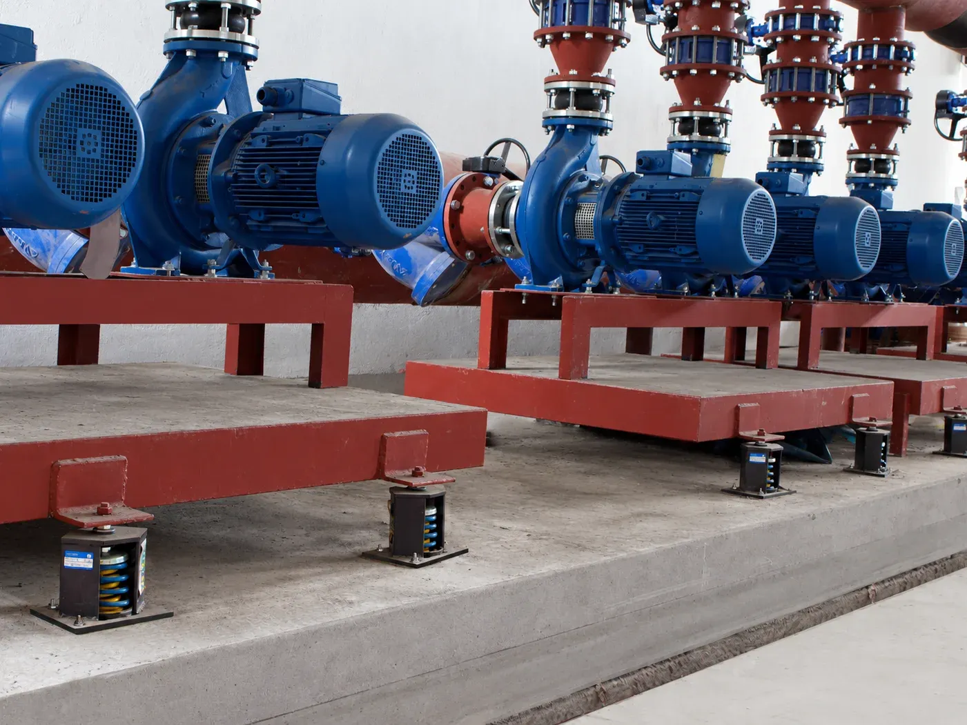 Pumps on red inertia bases in a mechanical plant room, each base on housed seismic spring isolators