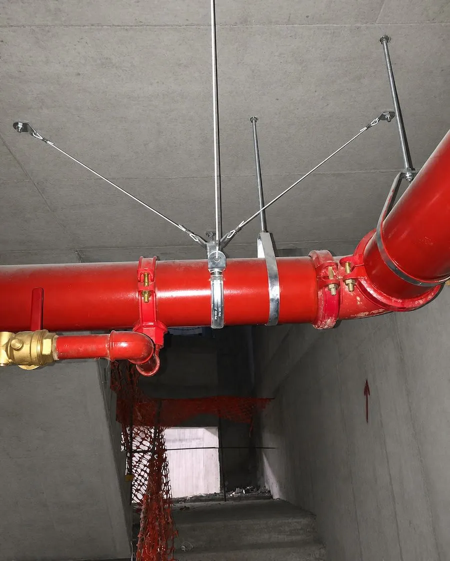 Four-way seismic sway brace on a sprinkler main — steel rods and wire ropes anchored to the concrete soffit