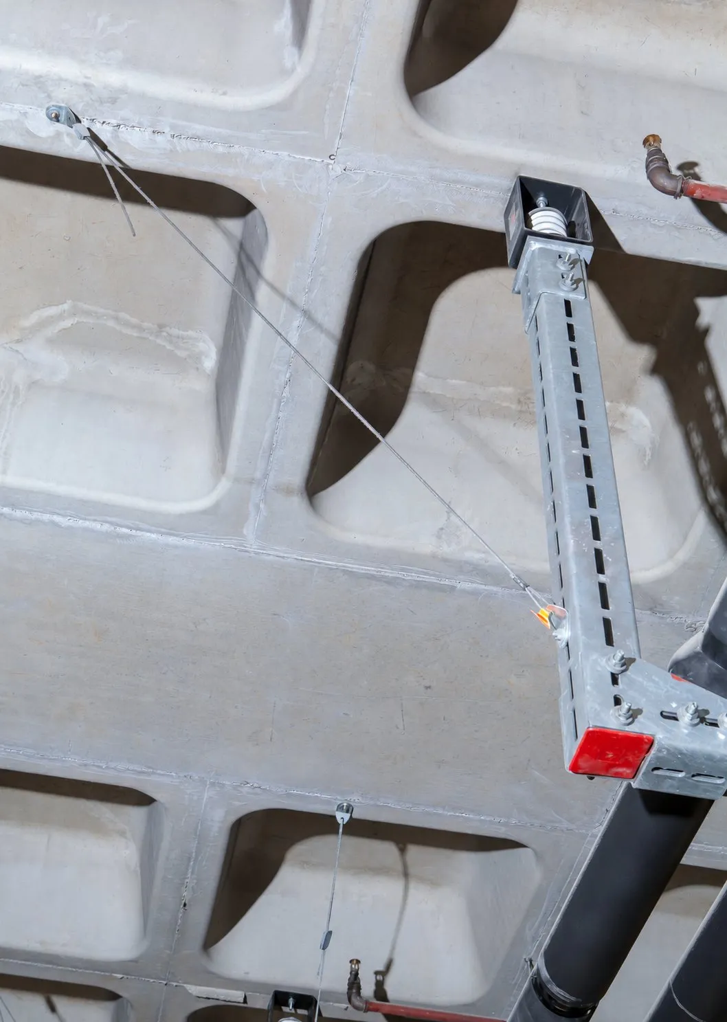 Spring hanger at the top of an isolated trapeze, with a seismic cable restraint anchored to the slab