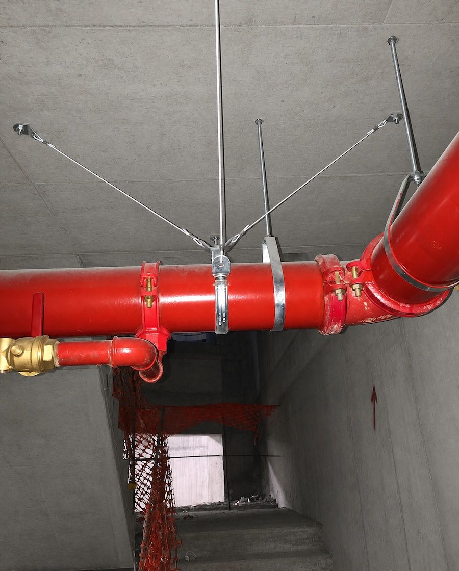 Four-way seismic sway brace on a sprinkler main &mdash; steel rods and wire ropes anchored to the concrete soffit